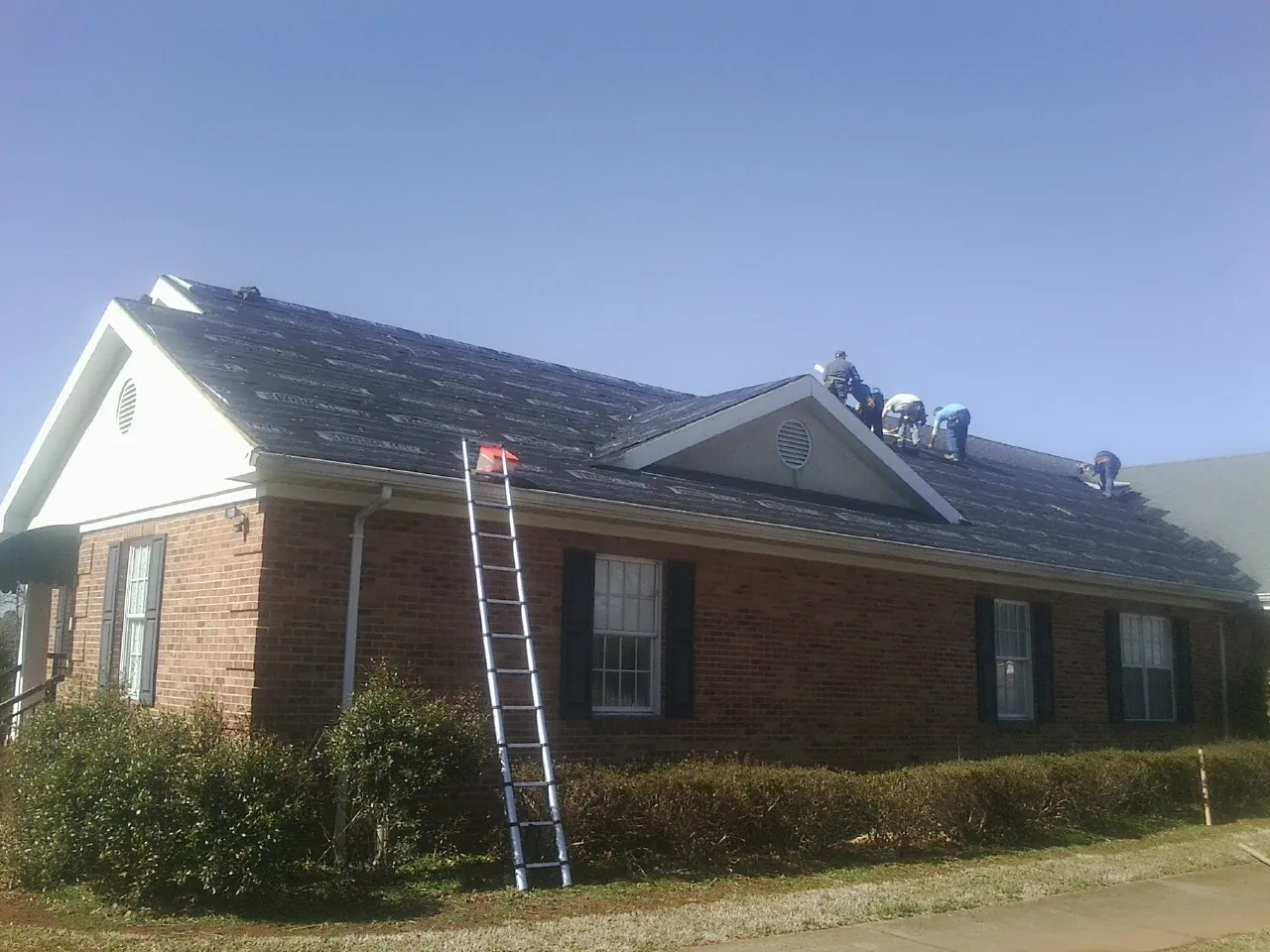 Crew tearing shingles off a brick ranch roof with a ladder set — Emergency Roof Repair work by our crew in Ringgold