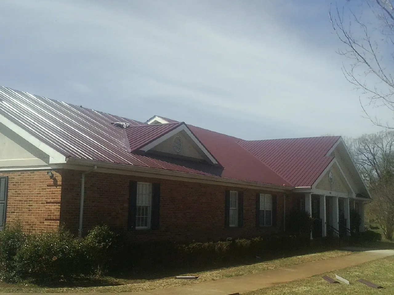Red metal roof with gabled entries on a long brick building, from a Hail Damage Roof Repair job in Ringgold