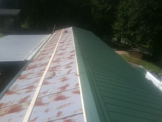 Old rusted panels beside newly installed green metal roofing — Wind Damage Roof Repair by Roofing Brothers in Ringgold