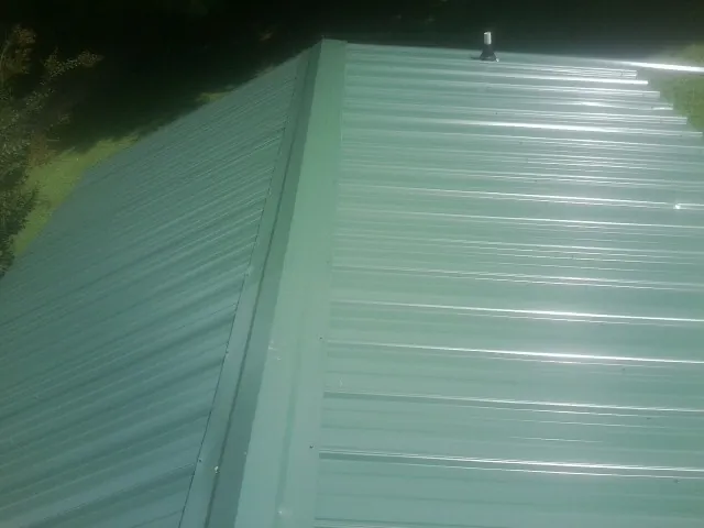 New green metal panels meeting at the ridge of a roof — Flat Roof Repair work by our crew in Ringgold
