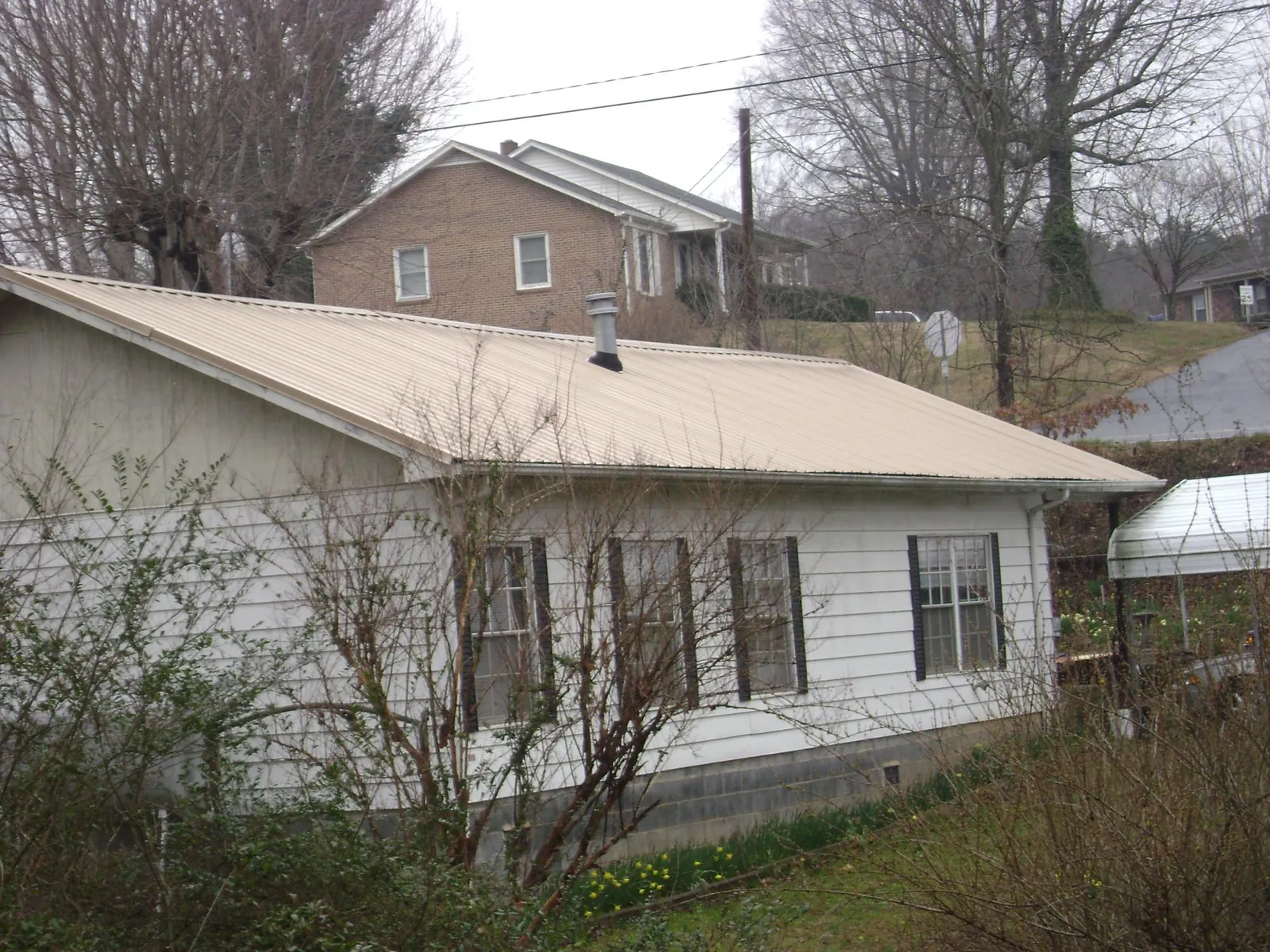 Tan metal roof on a white sided house set into a hillside — Commercial Roofing by Roofing Brothers in Ringgold
